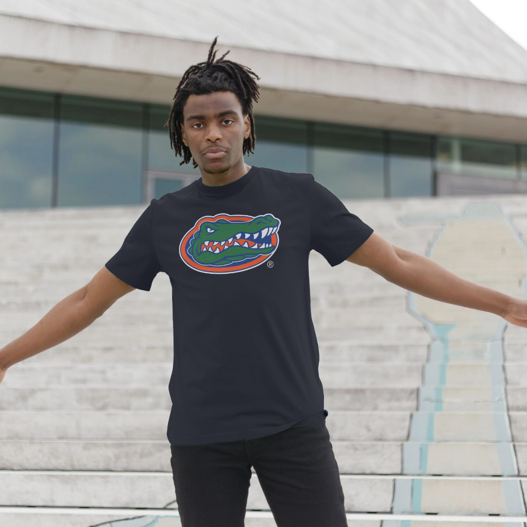 A man wearing a black t-shirt with a Florida Gators alligator logo on the chest, standing on outdoor concrete steps with his arms outstretched.